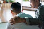 two men sit facing away, one has his arm on the other's shoulder