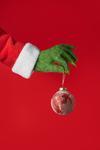the grinch's humanoid paw pinches the string of a bauble